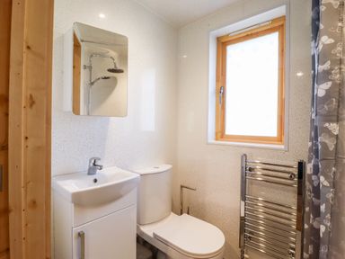 A bathroom with a sink, toilet, mirror, window, towel radiator, and a shower curtain at Clover Lodge in Theberton near Leiston