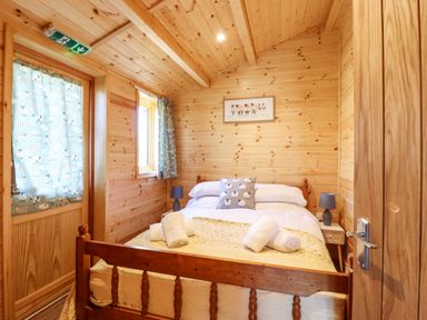 A wooden bedroom with a double bed windows curtains and two bedside lamps at Clover Lodge in Theberton near Leiston