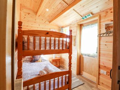 A small bedroom with bunk beds wooden walls a side table window and door at Clover Lodge Theberton near Leiston