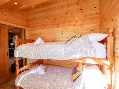 A wooden bunk bed with patterned bedding and rolled towels in a wood-paneled room at Clover Lodge Theberton near Leiston