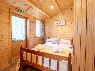A small bedroom with wooden walls and ceiling a bed with white linens and rolled towels at Clover Lodge in Theberton near Leiston