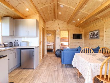 An open wooden interior with a kitchen area on the left a dining table with chairs on the right and a blue sofa in the center at Clover Lodge Theberton near Leiston
