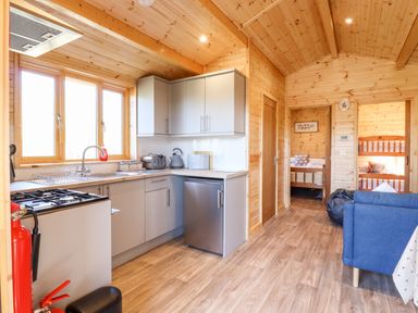 A kitchen with cabinets sink fridge and stove next to a living area with blue sofa and two bedrooms visible at Clover Lodge Theberton near Leiston