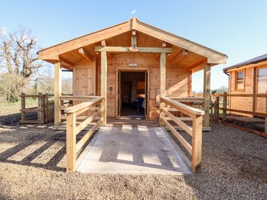 A wooden cabin with a ramp and railing outside surrounded by gravel at Clover Lodge Theberton near Leiston