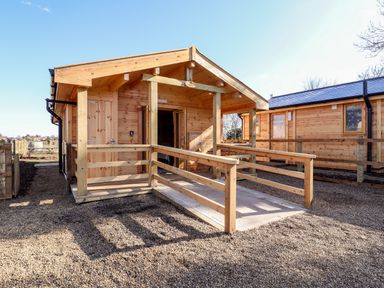 A wooden cabin with a ramp and porch at Clover Lodge Theberton near Leiston