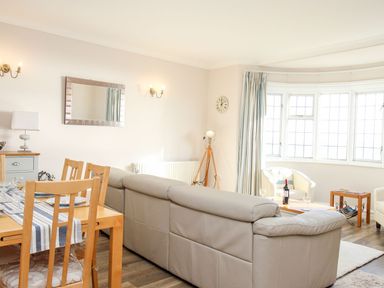 A living room and dining area with wooden chairs a beige sofa and bay windows at Ocean Watch 5 in Greenhill