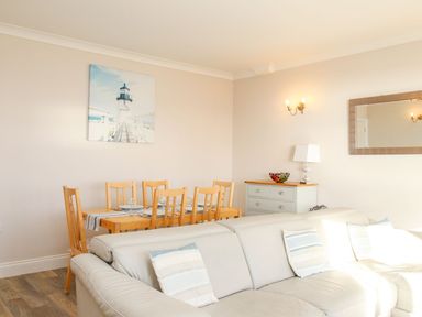 A dining area with wooden chairs and table next to a white sofa with cushions in a living room at Ocean Watch 5 in Greenhill