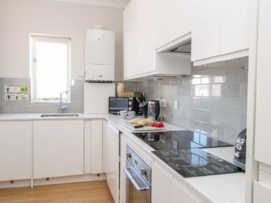 A kitchen with a sink, stove, oven, microwave, kettle, toaster, knives in a holder, bread rolls on a cutting board, and a window at Ocean Watch 5 in Greenhill