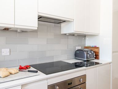 A kitchen countertop with a cutting board holding bread and red chili peppers a black toaster and a stovetop at Ocean Watch 5 in Greenhill