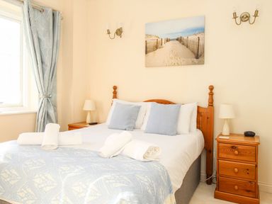 A bedroom with a wooden bed frame two nightstands with lamps rolled towels and a window with curtains at Ocean Watch 5 in Greenhill