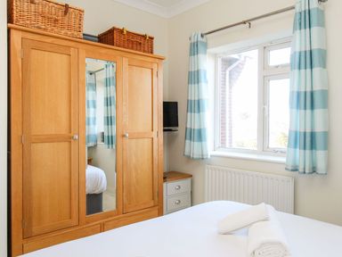 A bedroom with a wooden wardrobe a mirror striped curtains on a window and a bed with rolled towels at Ocean Watch 5 Greenhill