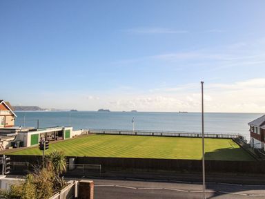 A green sports field beside the sea with ships in the water and buildings on either side at Ocean Watch 5 in Greenhill
