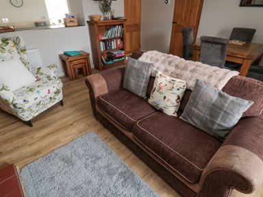 A living room with a brown sofa and patterned armchair a wooden bookshelf and dining table at Castle Keep in Norham