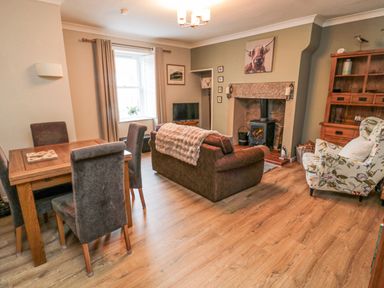 A living room with a dining table and chairs a sofa an armchair a fireplace with a wood burner and a wooden cabinet at Castle Keep in Norham