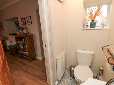 A small bathroom with a toilet a window with plants and an air freshener and a hallway with a wooden shelf filled with books at Castle Keep in Norham