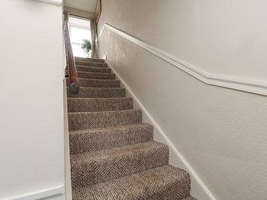 A carpeted staircase with a wooden handrail and a window with curtains and a plant at Castle Keep in Norham