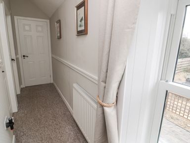 A narrow hallway with carpet a radiator two framed pictures closed doors and a window with curtains at Castle Keep in Norham