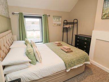 A bedroom with a double bed with green cushions and throw and folded towels on top at Castle Keep in Norham