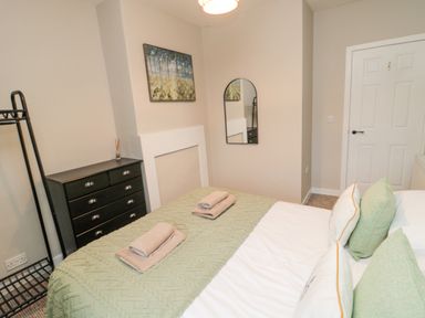 A bedroom with a bed covered in a green blanket and towels on top a black chest of drawers a wall mirror and a painting at Castle Keep in Norham