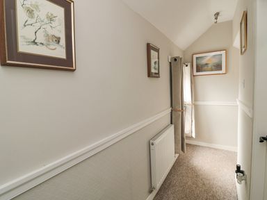 A narrow hallway with a radiator below a chair rail a window with curtains and framed pictures on walls at Castle Keep in Norham