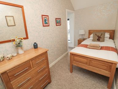 A bedroom with a single bed a wooden dresser with a mirror and decorative items at Castle Keep in Norham