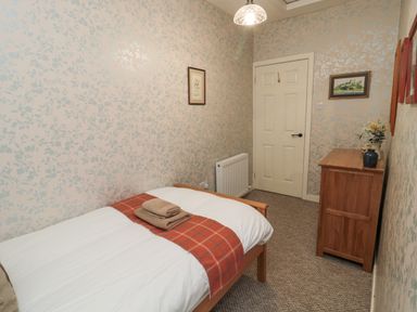 A bedroom with a single bed a wooden dresser and framed pictures on floral wallpapered walls at Castle Keep in Norham