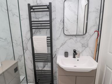 A bathroom with a sink, mirror, black towel rack holding a white towel, soap dispenser, and marble patterned walls at Castle Keep in Norham