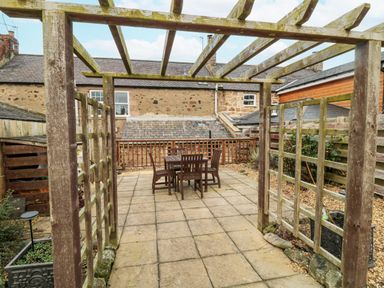 An outdoor patio with a wooden pergola and a table with four chairs at Castle Keep in Norham
