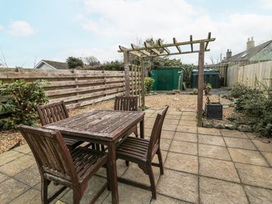 A garden with wooden table and chairs on a paved patio with a wooden pergola and a green shed at Castle Keep in Norham