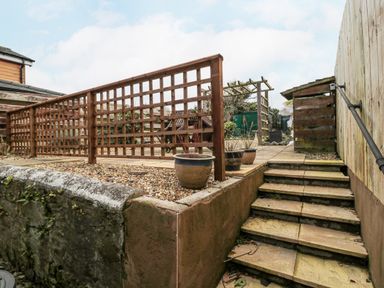 An outdoor garden area with stone steps leading up to a patio with wooden lattice fencing and plant pots at Castle Keep in Norham