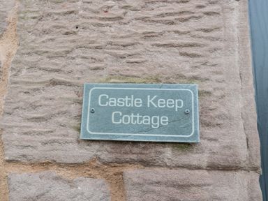 A stone wall with a rectangular sign reading Castle Keep Cottage at Castle Keep in Norham