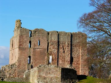 A stone ruin structure with narrow windows and a large tree on the right at Castle Keep in Norham