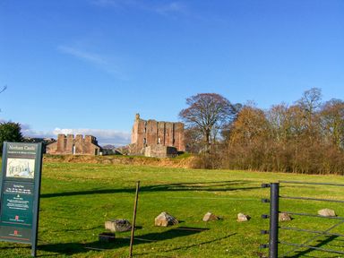 Ruins of Norham Castle with a sign and green grass in Norham