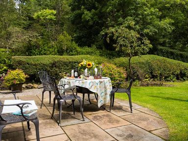 A garden patio with a table set for dining surrounded by chairs and green hedges at The Old Post House at Low Stott Park in Low Stott Park near Newby Bridge