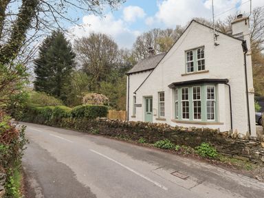 A white house with green window frames and door beside a road with stone wall at The Old Post House at Low Stott Park near Newby Bridge