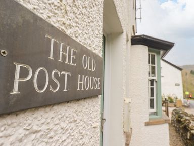 A close up of a plaque with The Old Post House on the exterior wall of a white textured building at The Old Post House at Low Stott Park near Newby Bridge