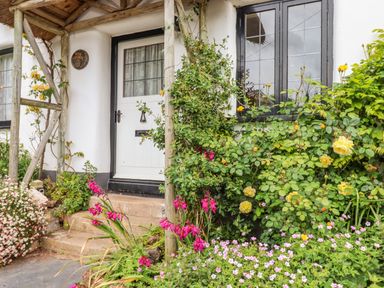 The entrance to a cottage with a white door black framed windows and flowers in the garden at Rose Cottage in Holcombe in Teignmouth