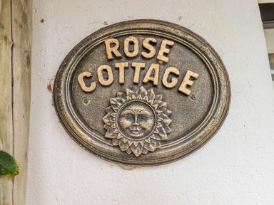 A wall plaque with the words Rose Cottage and a sun face decoration at Rose Cottage in Holcombe Teignmouth