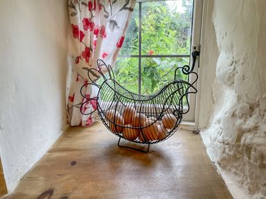 A chicken-shaped wire basket with brown eggs on a wooden windowsill with floral curtains at Rose Cottage in Holcombe in Teignmouth
