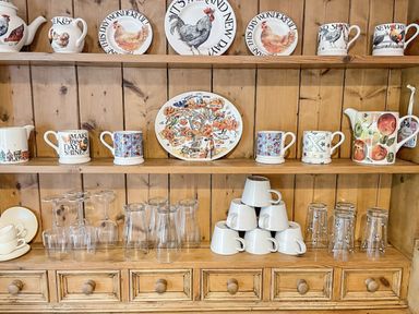 Wooden kitchen shelves displaying decorative plates, mugs, glassware, and a teapot at Rose Cottage in Holcombe Teignmouth