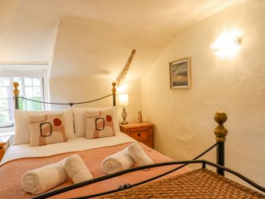 A bedroom with a double bed with rolled towels and pillows a bedside table with a lamp and a small owl figure at Rose Cottage in Holcombe Teignmouth