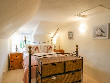 A bedroom with a metal bed frame wooden bedside tables lamps and wicker storage baskets at Rose Cottage in Holcombe Teignmouth