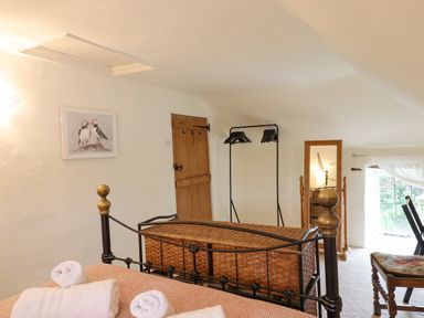 A bedroom with an iron bed, wicker trunk, wooden door, standing mirror, and clothes rack at Rose Cottage in Holcombe Teignmouth