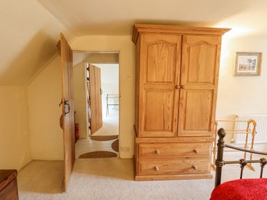 A wooden wardrobe next to an open wooden door inside a bedroom at Rose Cottage in Holcombe Teignmouth