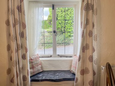 A window seat with two cushions and patterned curtains at Rose Cottage in Holcombe Teignmouth