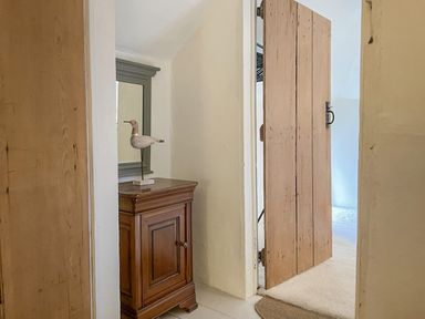 A wooden cabinet with a bird sculpture on top near a wall mirror and a partially open wooden door at Rose Cottage in Holcombe in Teignmouth