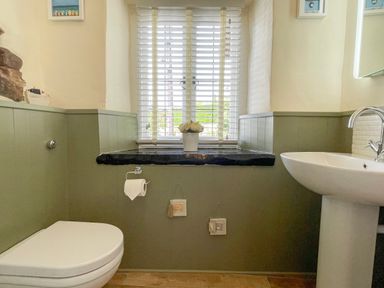 A bathroom with a toilet, sink, window with blinds, and decorative items on the wall at Rose Cottage in Holcombe Teignmouth