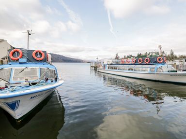 Two boats docked on a lake with hills and trees in the background at Claife Heights in Windermere