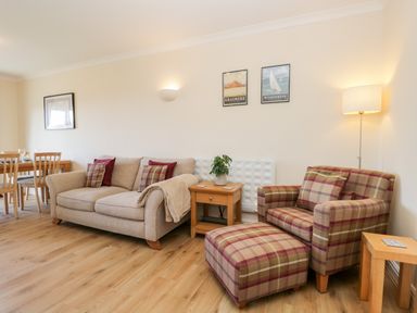 A living room with a beige sofa and a plaid armchair with matching footstool at Claife Heights in Windermere