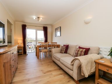 A living room with a beige sofa and wooden dining table near a sliding glass door at Claife Heights in Windermere